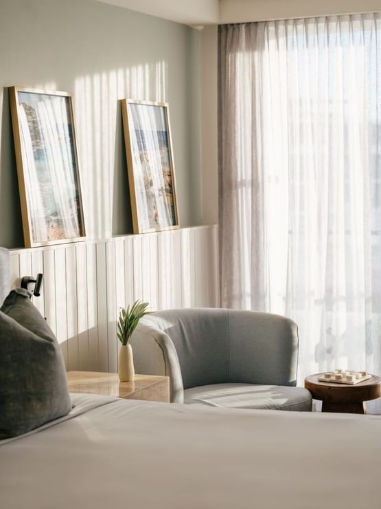 Sunset View King at Elysium Manly, showcasing two coastal artworks on a white wall above a grey armchair & wooden side table