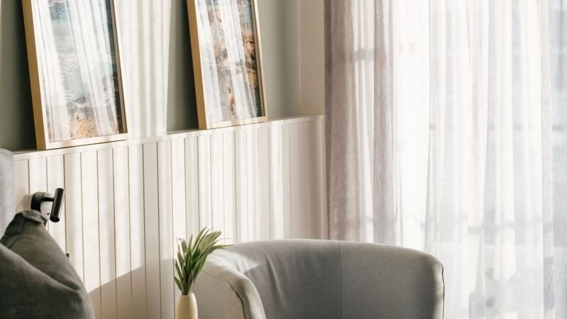Sunset View Two Bedroom at Elysium Manly, showcasing two coastal artworks on a white wall above a grey armchair & side table