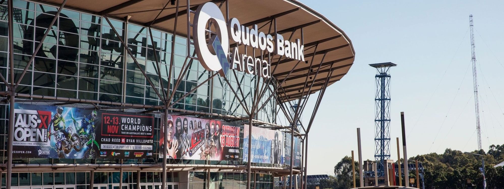 Exterior of the Quodos Bank Arena with banners and a clear sky in the background.