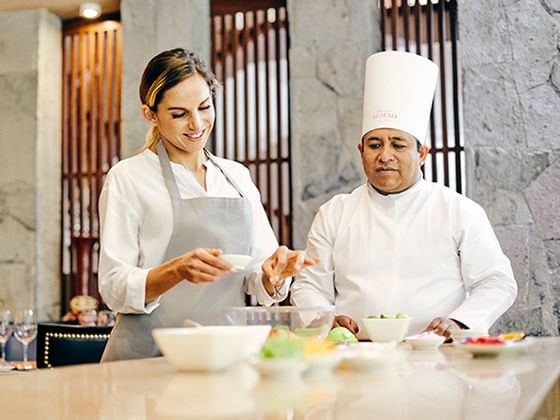 A chef guiding a lady with an apron to cook at Hotel Sumaq