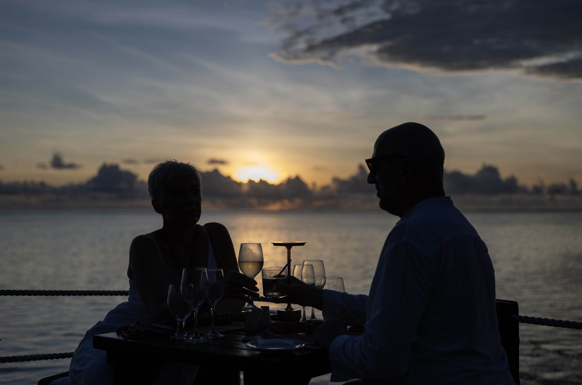 Couple dining by a wooden table under a cloudy sunset near the calm ocean in Wicked Walu at Warwick Fiji Resort and Spa