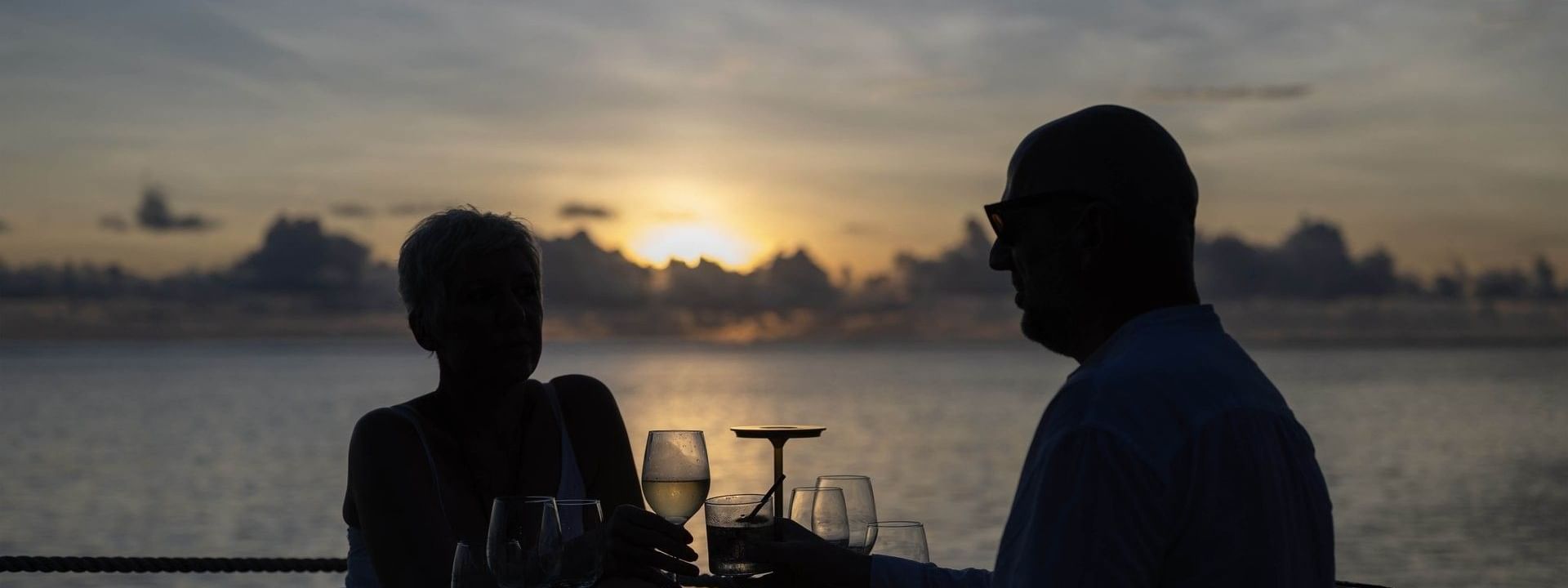Couple dining by a wooden table under a cloudy sunset near the calm ocean in Wicked Walu at Warwick Fiji Resort and Spa