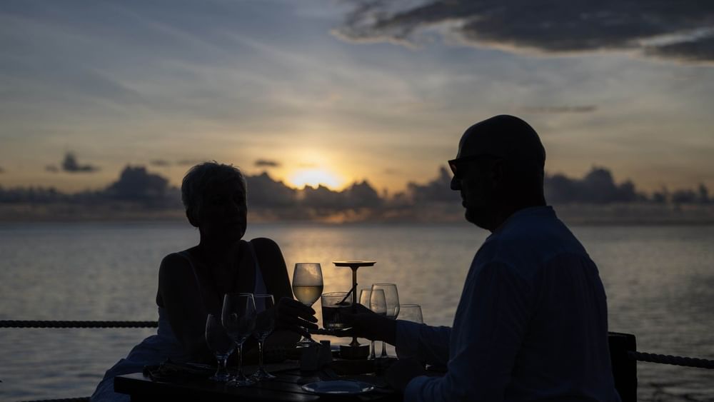 Couple dining by a wooden table under a cloudy sunset near the calm ocean in Wicked Walu at Warwick Fiji Resort and Spa