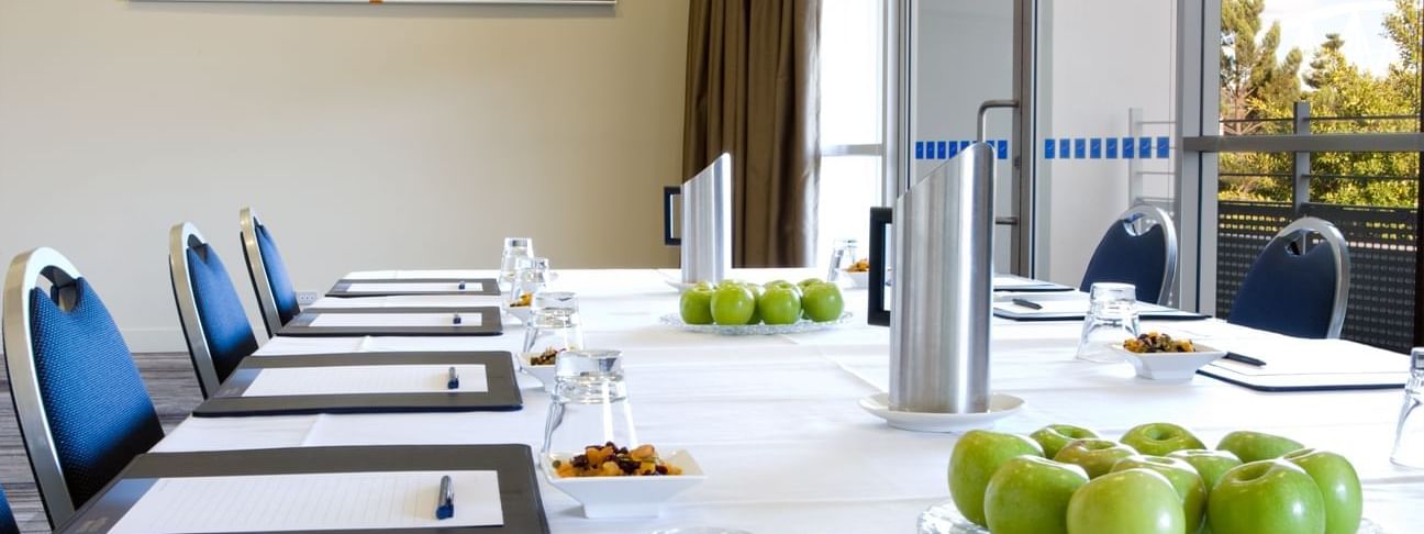 Boardroom set-up with notebooks, water glasses, and green apples in Forest Room at Novotel Sydney Olympic Park