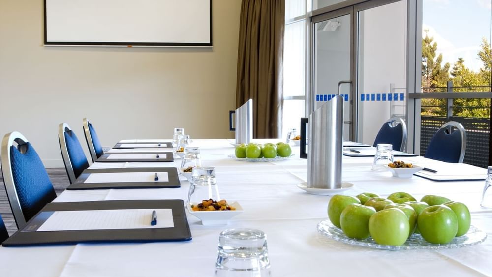 Boardroom set-up with notebooks, water glasses, and green apples in Forest Room at Novotel Sydney Olympic Park