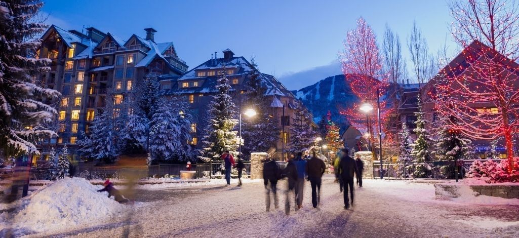 Evening view of Whistler Village with snow-covered streets and glowing holiday lights.