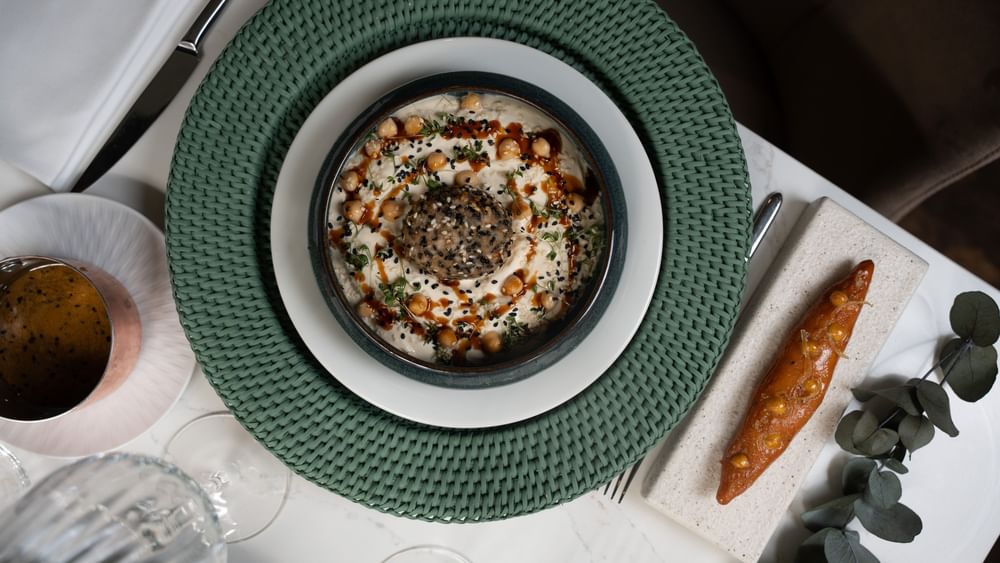 Bowl of creamy hummus topped with sesame seeds, & roasted carrot served in Le Céladon at Hotel Westminster Paris