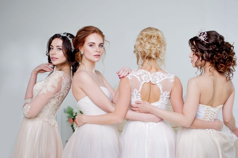 Four women in elegant, white bridal gowns pose gracefully together from behind at Warwick Melrose Dallas
