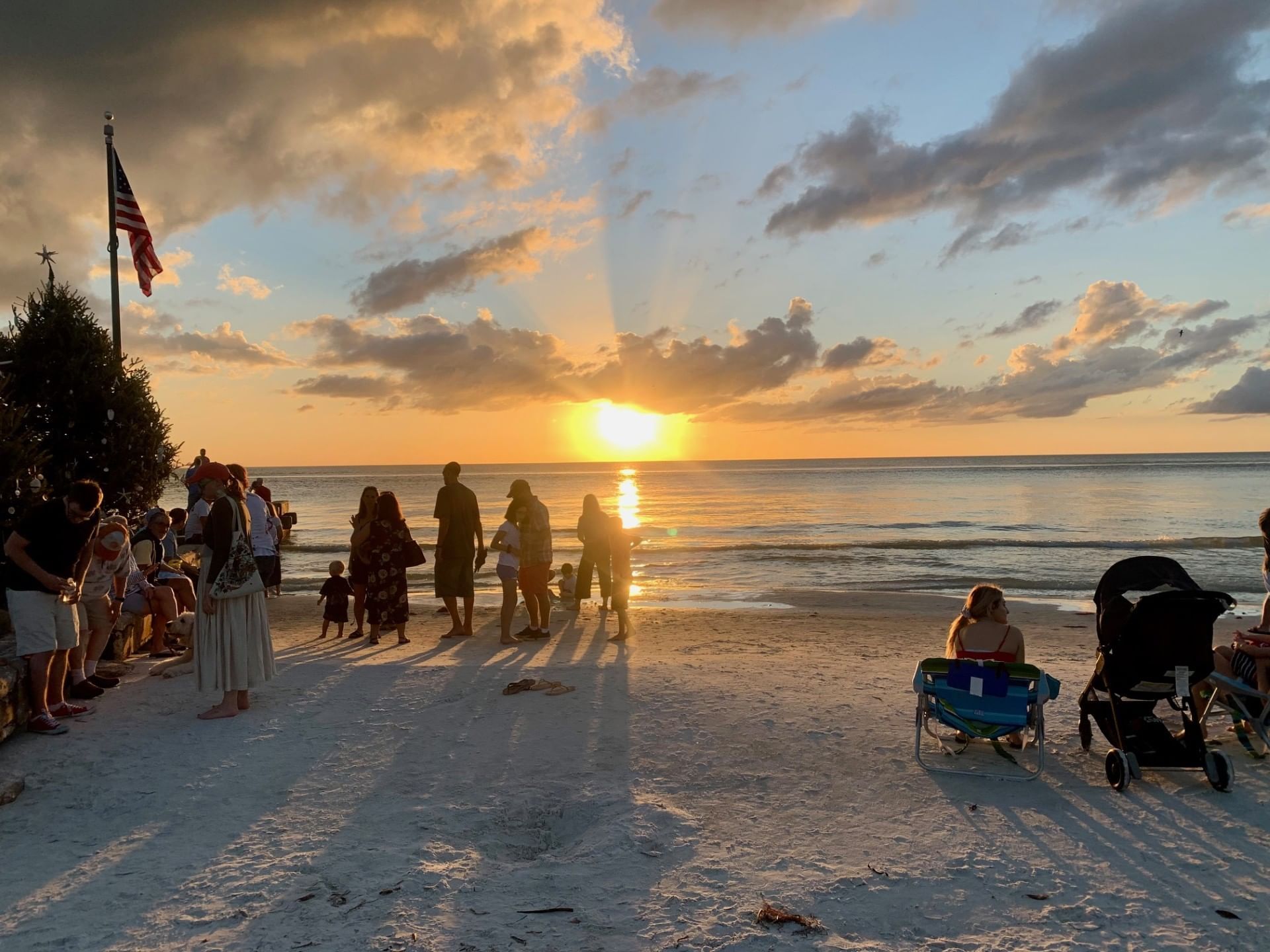 A crowd of people and an American flag silhouetted on a beach at sunset.