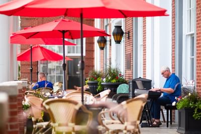 Musician playing a keyboard by a brick wall under large red patio umbrellas at Rodd Charlottetown Hotel