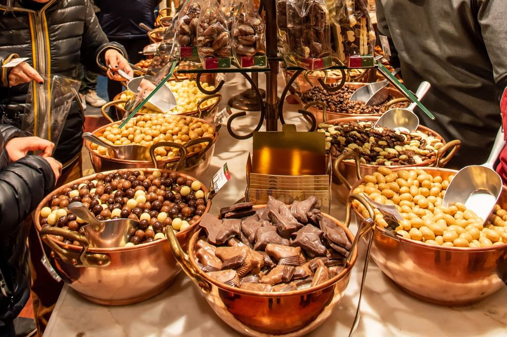 Copper bowls filled with various chocolates placed in rows, with metal scoops by the sweets at Warwick Grand Place Brussels