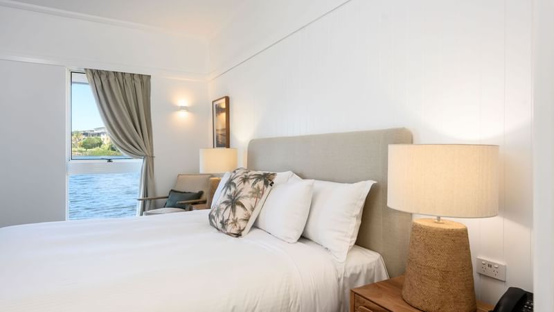 Bed by the nightstands and a window overlooking the water in the Deluxe Overwater Bungalow at Novotel Sunshine Coast Resort