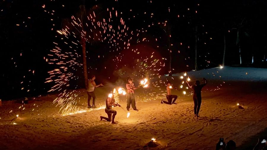 Performers with lit torches create a spectacle on the beach at night.