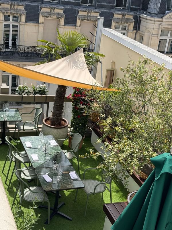 Rooftop terrace dining area with green chairs, potted plants, and shade sails at Warwick Paris Champs Elysées