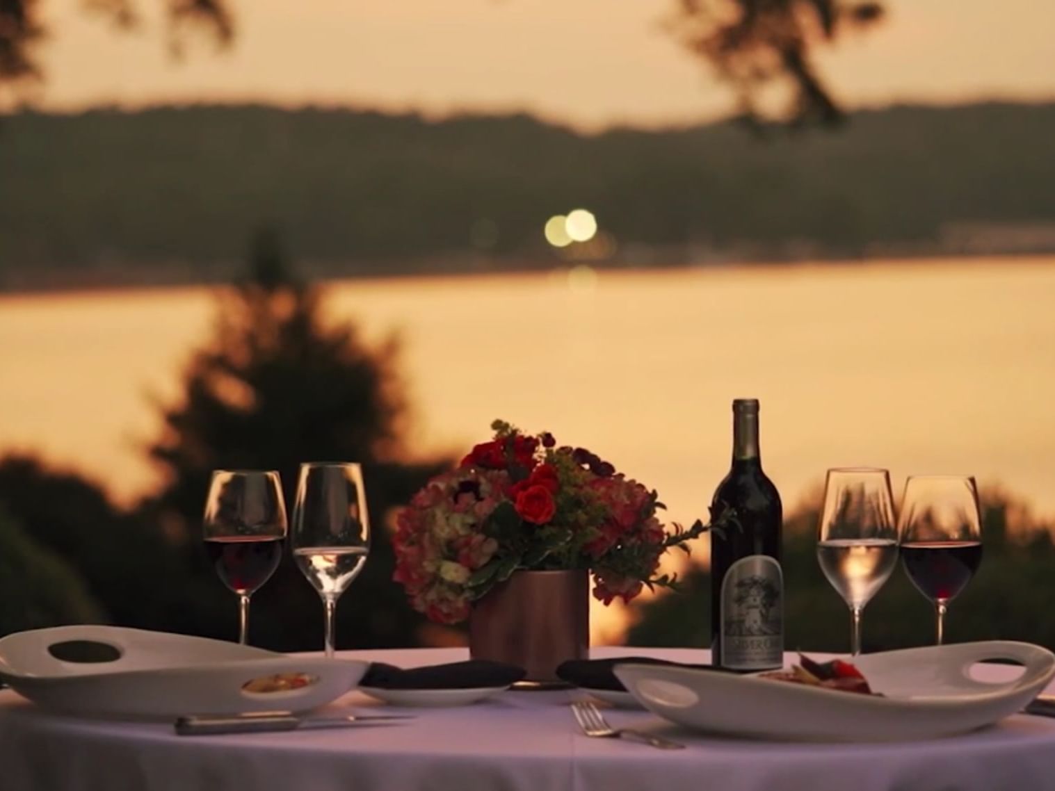 view of lake at sunset with wine, food, and flowers