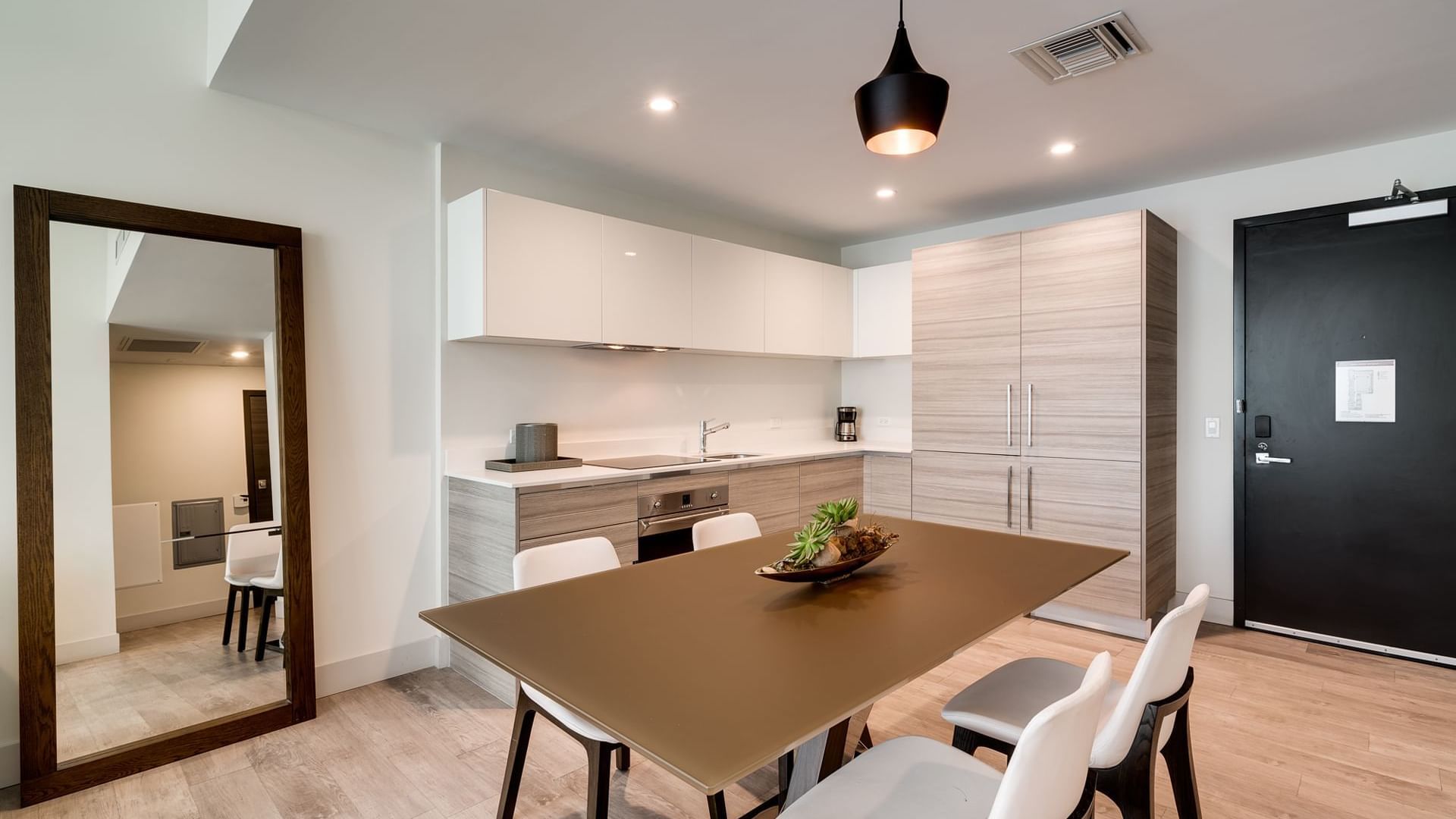 A modern kitchen and dining area with a brown table, white chairs, and a kitchenette.