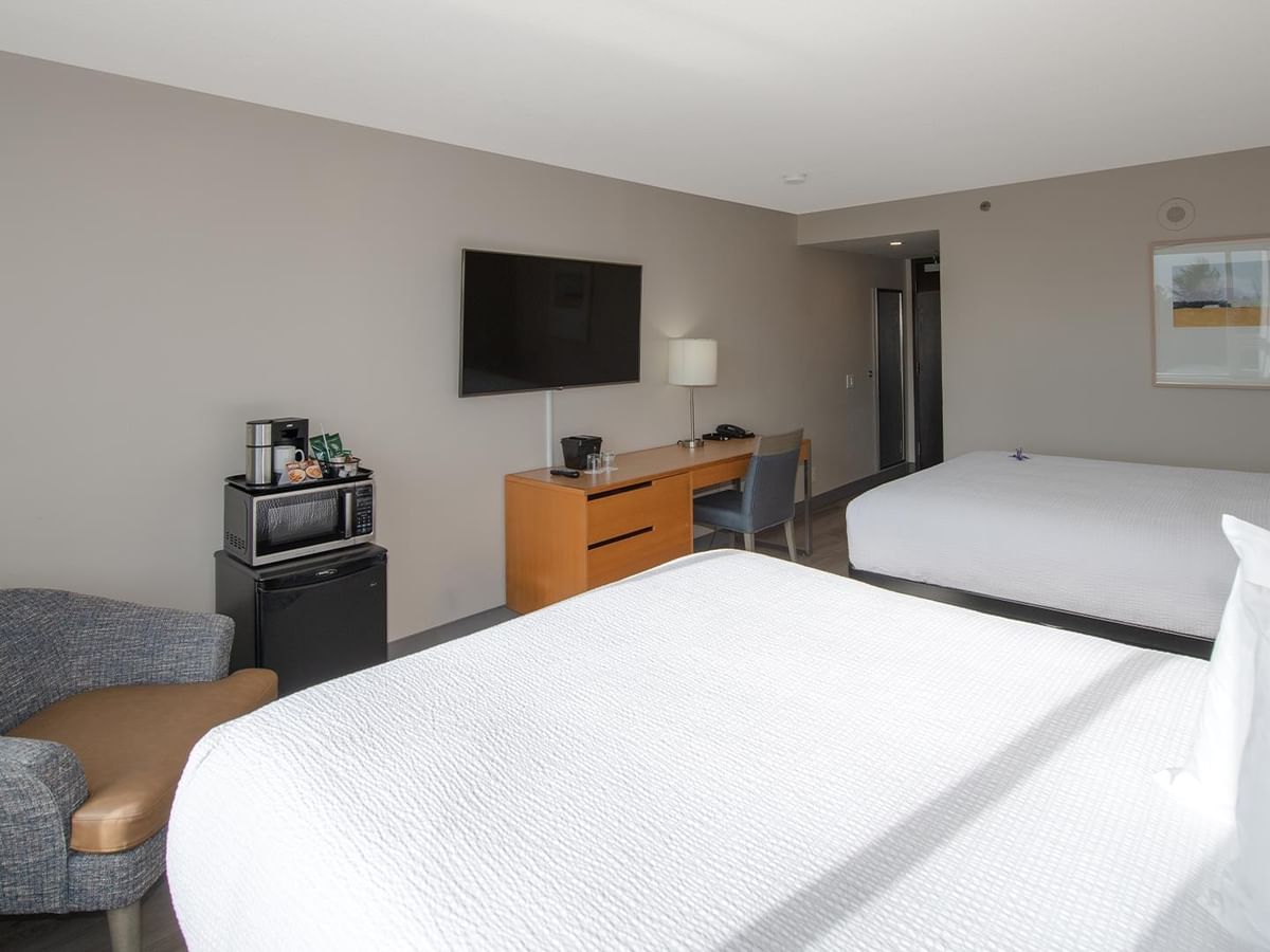 Room with two queen beds, a desk, TV, mini fridge, microwave and a chair .