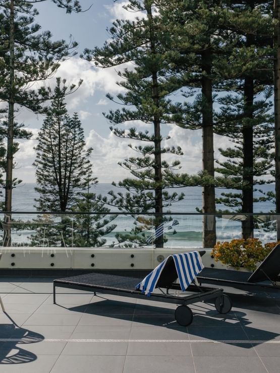 Elysium Suite at Elysium Manly, featuring black lounge chairs by a dining set under tall trees, with surrounding ocean views