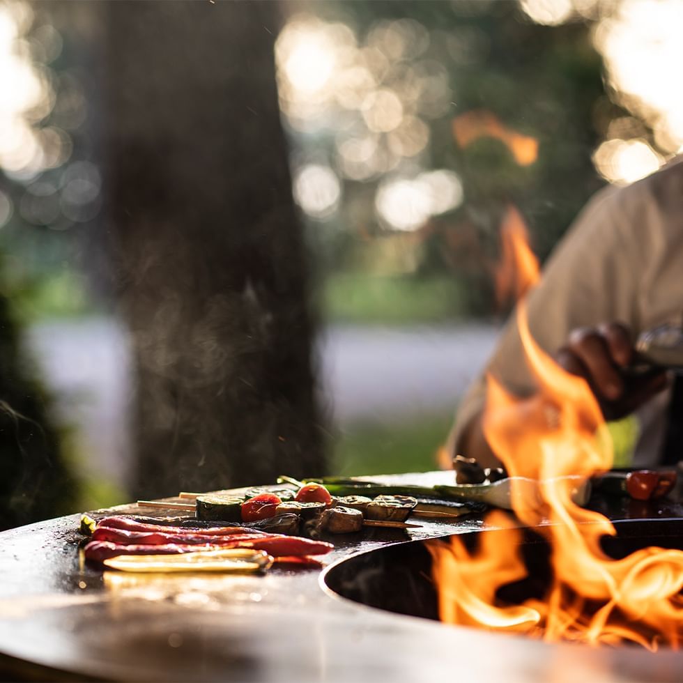 Live Cooking unter freiem Himmel mit brennendem Feuer und Speisen auf Grill.