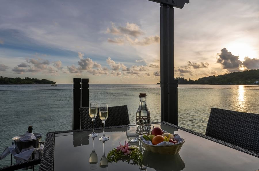 Outdoor dining table with wine, fruits, and ocean view at Warwick Le Lagon.