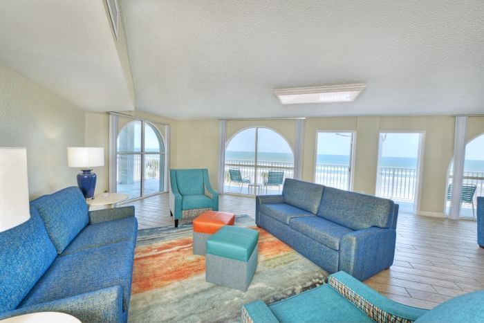 A wide view of a living room with blue couches, armchairs, and a balcony with an ocean view.