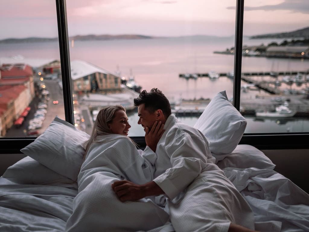 Couple cuddling on abed with bay view, Grand Chancellor Hobart