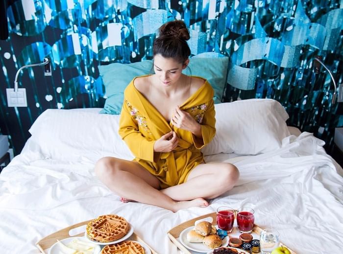 Donna seduta sul letto con vassoi di colazione a DUPARC Contemporary Suites