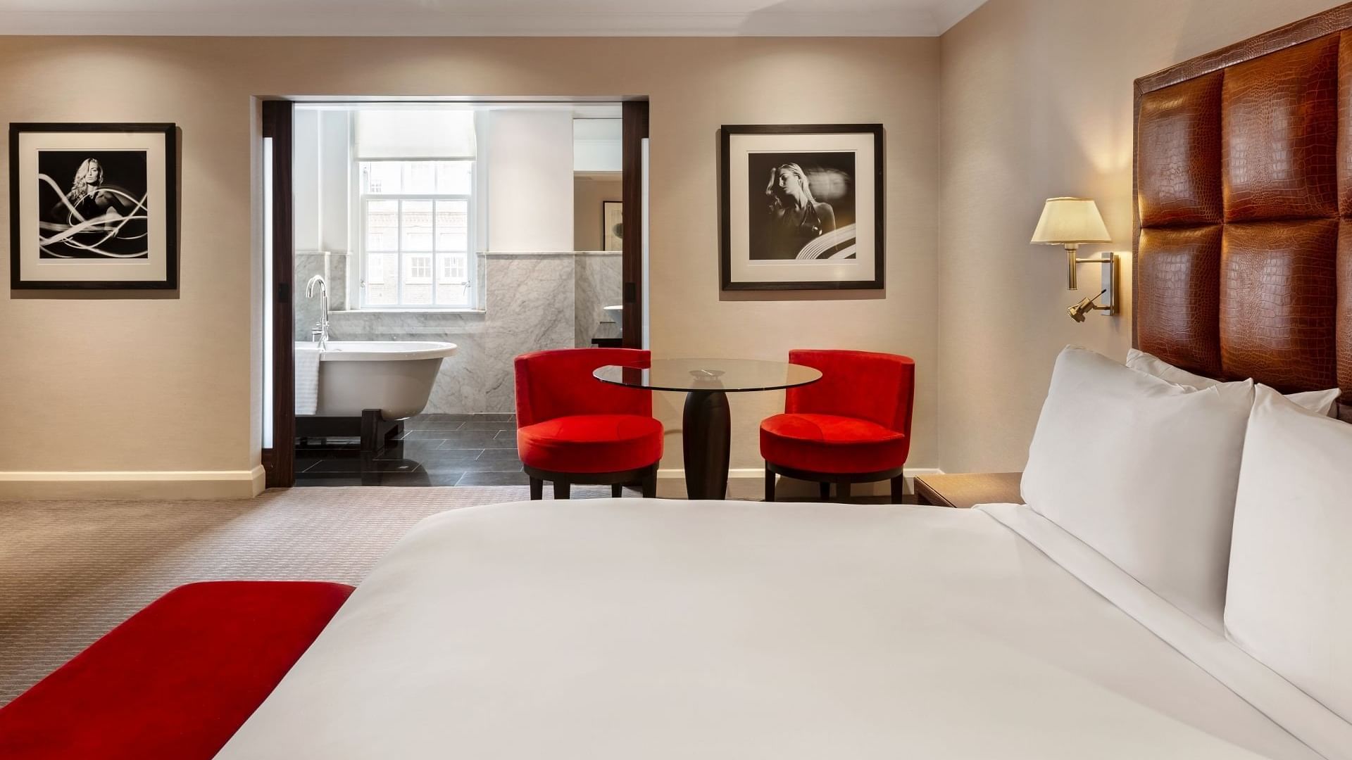 Modern Collection Premium Room at The May Fair Hotel with a plush bed, red accents, and a round glass table with red chairs