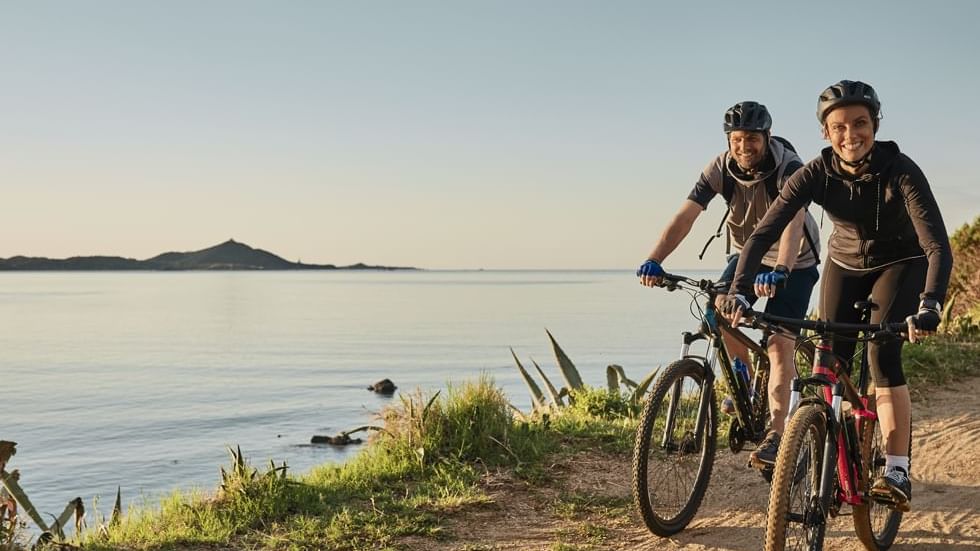 A couple cycling by a river near Falkensteiner Hotels