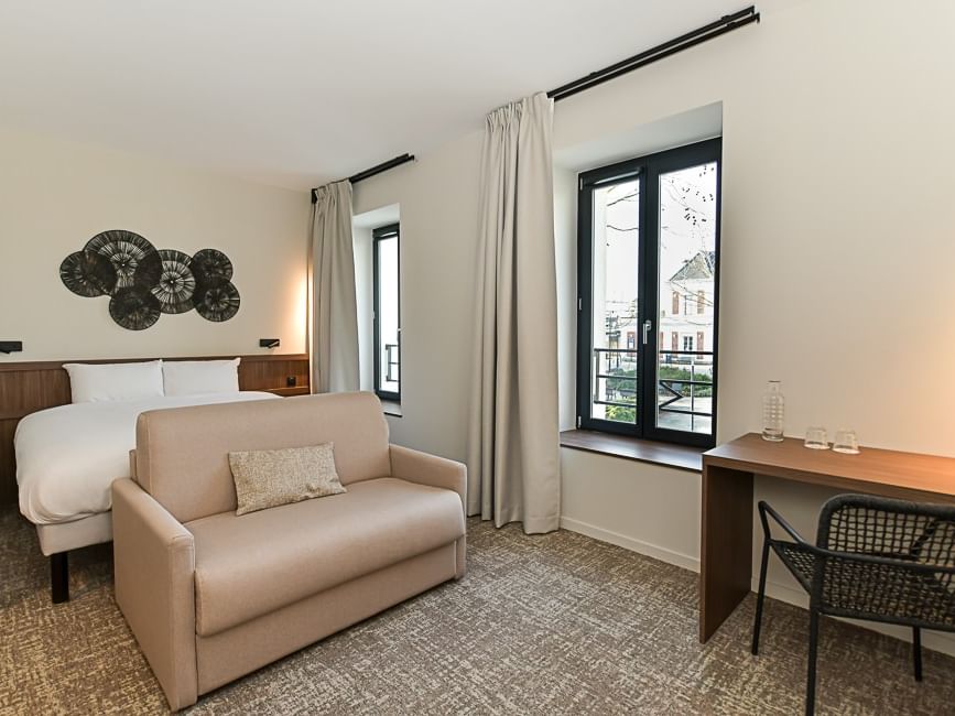 Chambre moderne avec lit, canapé, bureau et fenêtre au Hôtel Rivella.