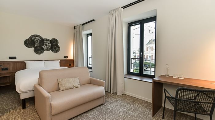 Chambre moderne avec lit, canapé, bureau et fenêtre au Hôtel Rivella.