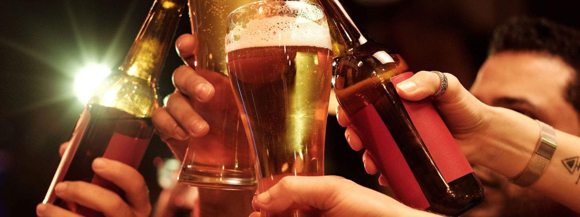 Friends toasting with beer bottles and glasses in a warm, festive atmosphere for end-of-year celebrations.