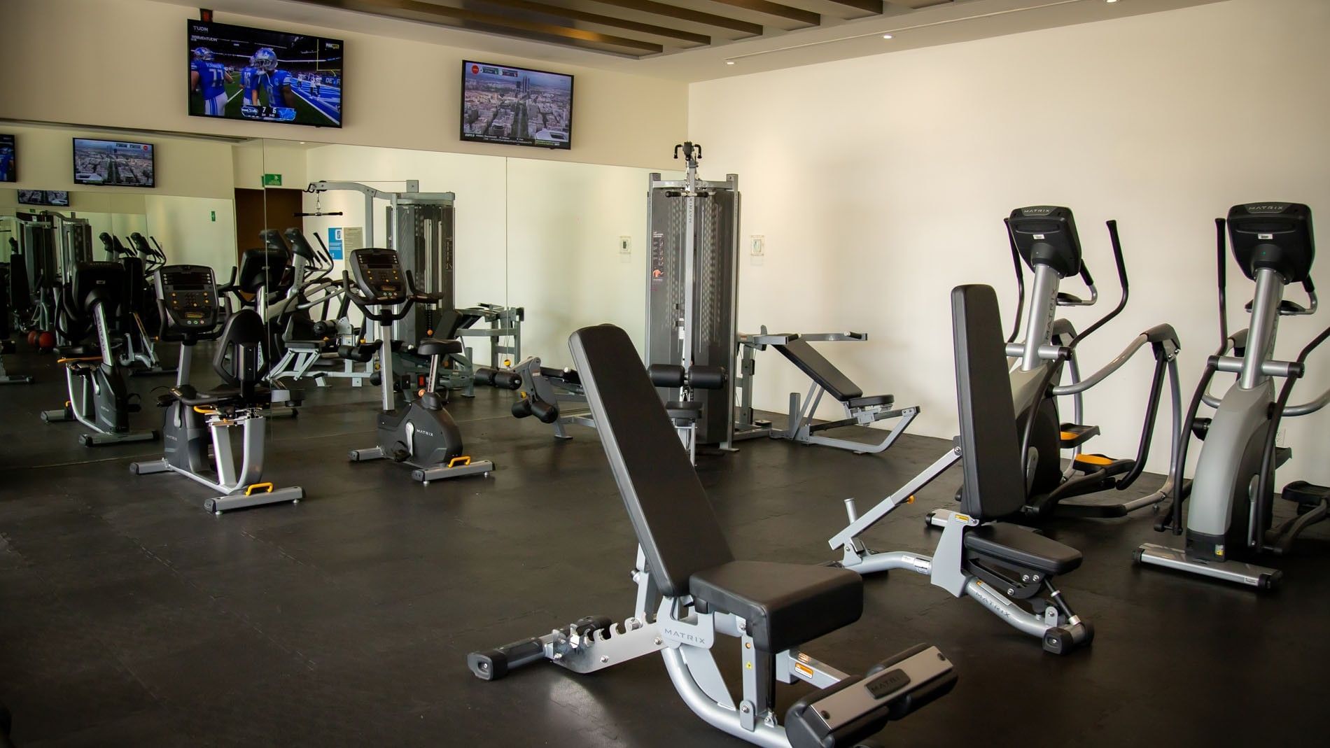 Fitness center with weight benches, strength machines, and TVs on the wall at Camino Real Fashion Drive, Monterrey