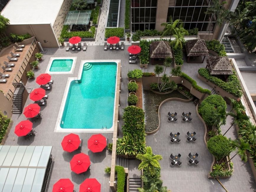 An aerial view of the outdoor pool area with bright red umbrellas and lush greenery at Carlton Hotel Singapore
