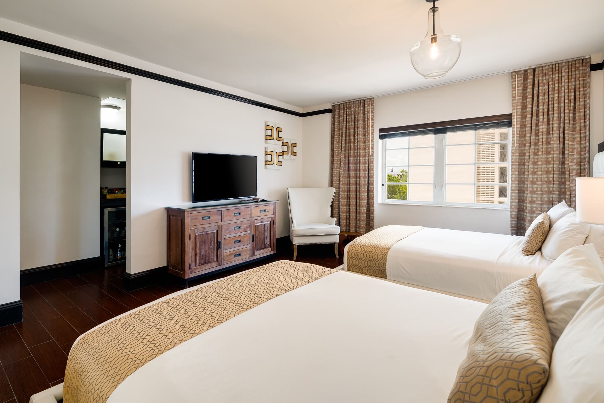 A hotel room with two beds, a TV on a dresser, a chair, and a window with curtains.