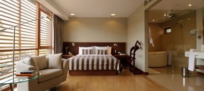 NOI Suite con cama a rayas, sofá y baño con paredes de vidrio en NOI Vitacura