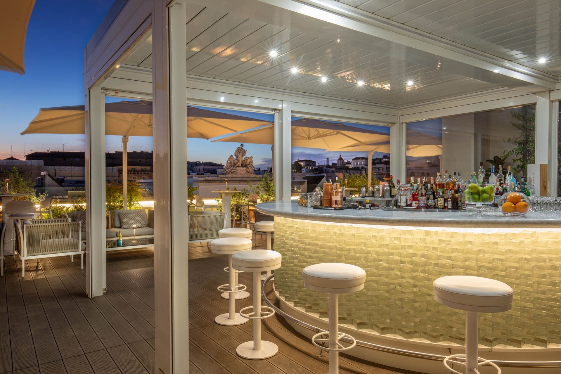 Rooftop bar featuring a glowing curved bar counter under umbrellas with a panoramic city view at The Glam Hotel