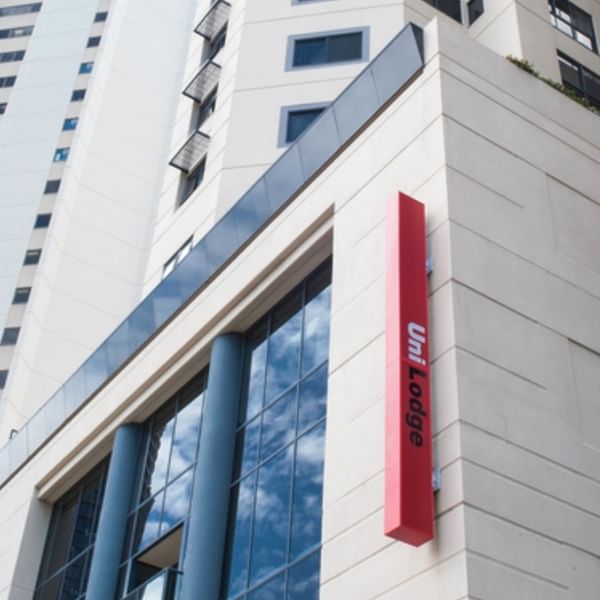 Modern white high-rise building exterior with glass windows and red UniLodge signage under clear blue sky
