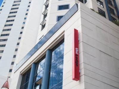 Modern white high-rise building exterior with glass windows and red UniLodge signage under clear blue sky
