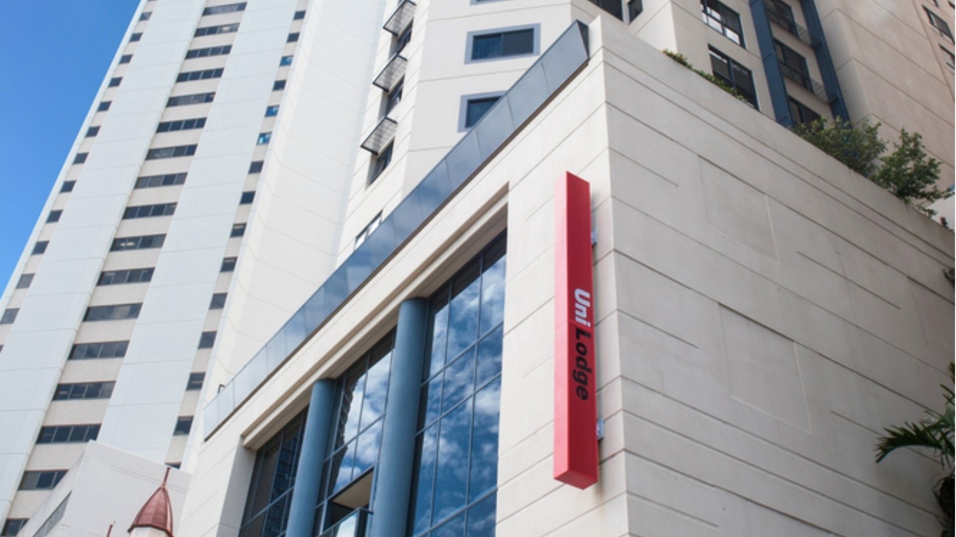 Modern white high-rise building exterior with glass windows and red UniLodge signage under clear blue sky