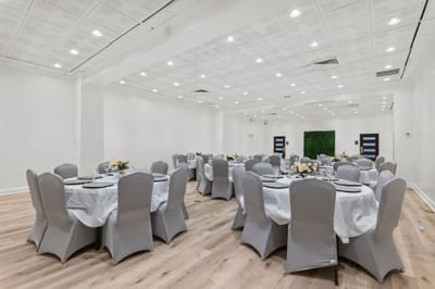 Elegant ballroom at The Riverwalk Plaza Hotel with round tables dressed in white tablecloths, chairs, and floral displays