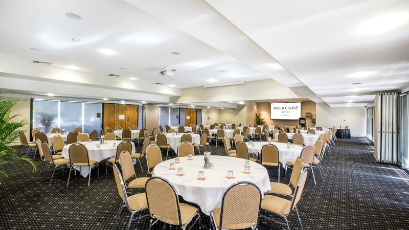 Interior of Ballroom featuring round tables with chairs, and a display screen at Mercure Hotel Townsville