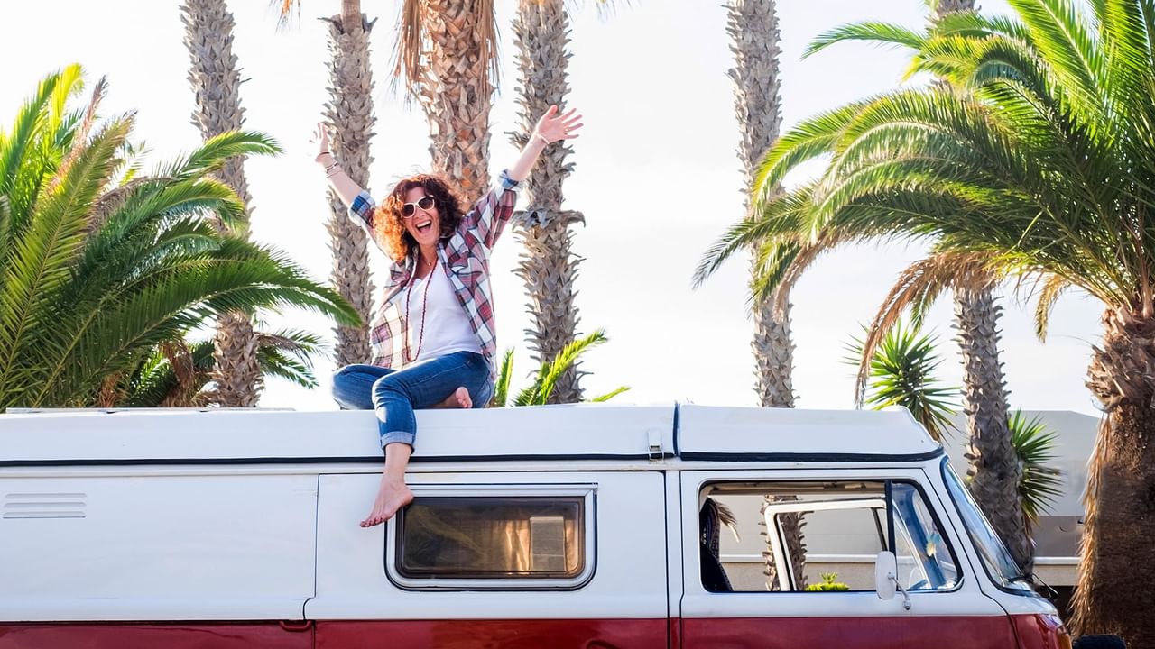 Woman sitting on van roof with arms raised