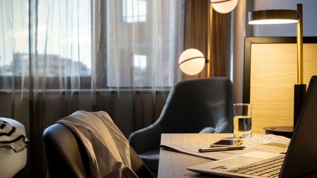 Laptop by a water glass on the table in the Executive King Room at Novotel Sydney Parramatta, under a desk lamp near window