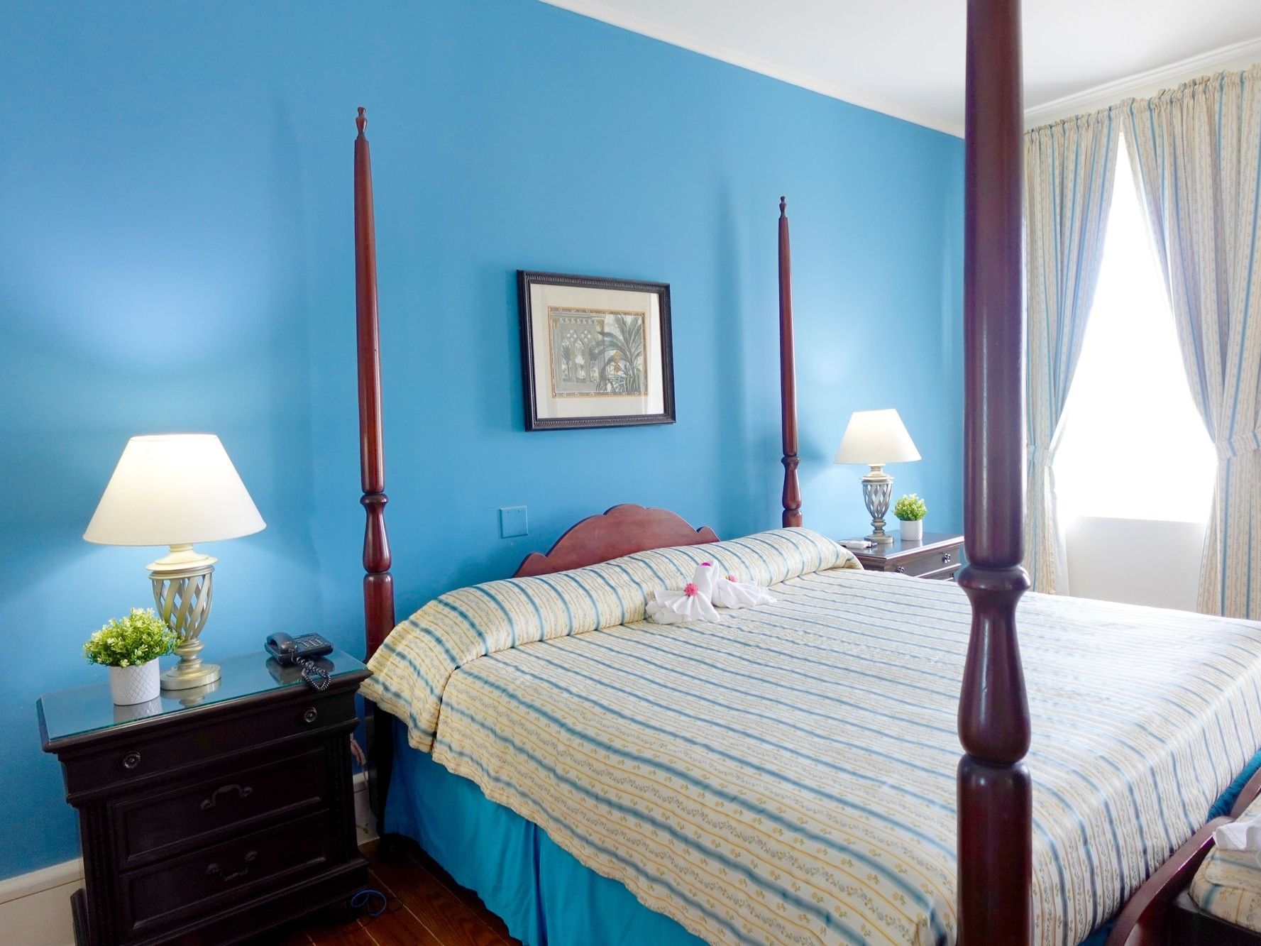 Heritage Room with blue walls, four-poster bed, striped bedding, and white curtains at Savannah Beach Hotel, Bridgetown.
