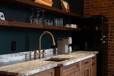 Kitchen with wooden shelves, marble countertop, and brass faucet in One Bedroom King Suite at The Delegate Hotel