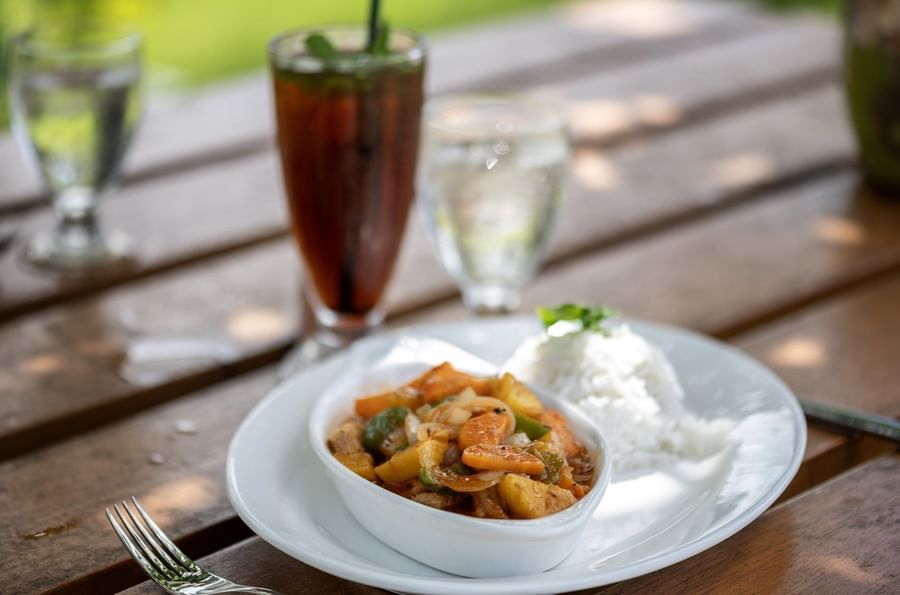 Savory chicken curry served with white rice on a plate by tall iced drink in Tambua Restaurant at Tambua Sands Beach Resort