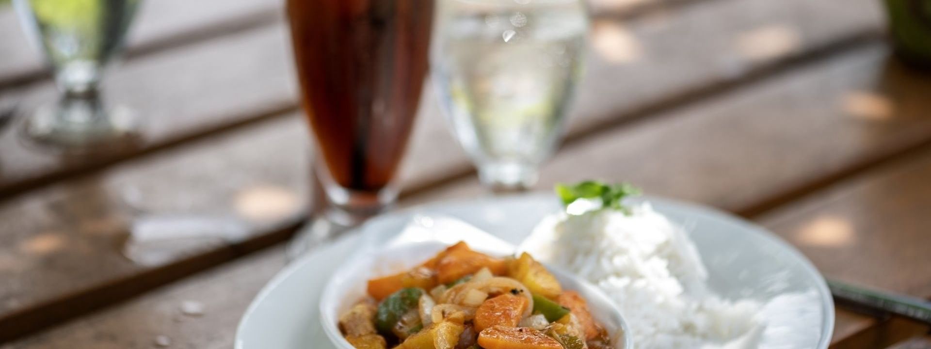 Savory chicken curry served with white rice on a plate by tall iced drink in Tambua Restaurant at Tambua Sands Beach Resort