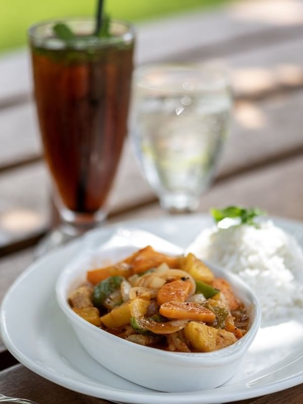 Savory chicken curry served with white rice on a plate by tall iced drink in Tambua Restaurant at Tambua Sands Beach Resort