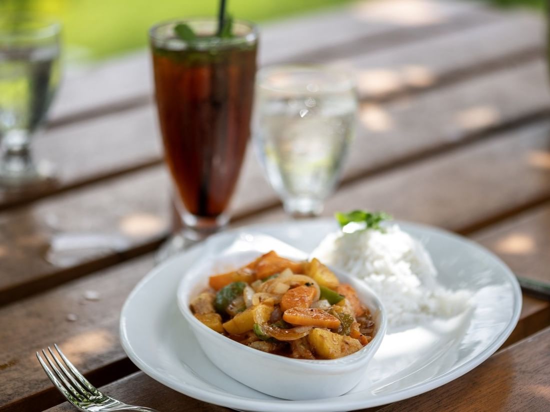 Savory chicken curry served with white rice on a plate by tall iced drink in Tambua Restaurant at Tambua Sands Beach Resort